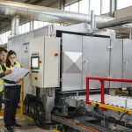 Tecnici accanto a un forno elettrico industriale su misura durante l'integrazione in linea con documentazione e quadro di controllo